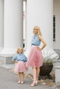 A beautiful young blonde mother and her charming daughter in the same romantic clothes stand near the columns and smile Royalty Free Stock Photo