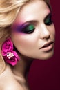 Beautiful young blonde woman with creative make-up color and flowers on the ears. Beauty face. Art makeup. Royalty Free Stock Photo