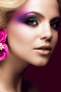 Beautiful young blonde woman with creative make-up color and flowers on the ears. Beauty face. Art makeup. Royalty Free Stock Photo