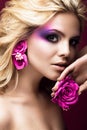 Beautiful young blonde woman with creative make-up color and flowers on the ears. Beauty face. Art makeup. Royalty Free Stock Photo