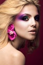 Beautiful young blonde woman with creative make-up color and flowers on the ears. Beauty face. Art makeup. Royalty Free Stock Photo