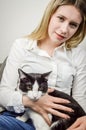 Beautiful young blonde woman cuddling a bored looking young black and white cat Royalty Free Stock Photo