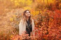 Beautiful young blonde woman in dress sitting with pensive look in tall grass in autumn forest