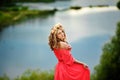 Beautiful young blonde woman with a flower wreath on her head. Beauty girl with flowers hairstyle in a red long dress near the Royalty Free Stock Photo