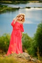 Beautiful young blonde woman with a flower wreath on her head. Beauty girl with flowers hairstyle in a red long dress near the Royalty Free Stock Photo