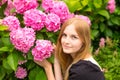 Beautiful young blonde woman with flowers near face. Pink Hydrangea macrophylla blooming in summer in botanical garden Royalty Free Stock Photo