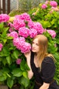 Beautiful young blonde woman with flowers near face. Pink Hydrangea macrophylla blooming in summer in botanical garden Royalty Free Stock Photo