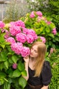 Beautiful young blonde woman with flowers near face. Pink Hydrangea macrophylla blooming in summer in botanical garden Royalty Free Stock Photo