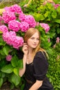 Beautiful young blonde woman with flowers near face. Pink Hydrangea macrophylla blooming in summer in botanical garden Royalty Free Stock Photo