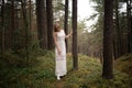 Walking Beautiful young blonde woman forest nymph in white dress in evergreen wood Royalty Free Stock Photo