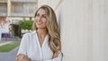 Beautiful young blonde woman happily standing at city street corner, confidently looking to the side with arms crossed, emanating Royalty Free Stock Photo