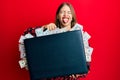 Beautiful young blonde woman holding briefcase full of dollars sticking tongue out happy with funny expression Royalty Free Stock Photo