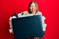 Beautiful young blonde woman holding briefcase full of dollars winking looking at the camera with sexy expression, cheerful and Royalty Free Stock Photo