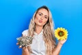 Beautiful young blonde woman holding sunflower seeds an flower looking at the camera blowing a kiss being lovely and sexy