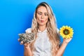 Beautiful young blonde woman holding sunflower seeds an flower making fish face with mouth and squinting eyes, crazy and comical Royalty Free Stock Photo