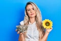 Beautiful young blonde woman holding sunflower seeds an flower relaxed with serious expression on face Royalty Free Stock Photo