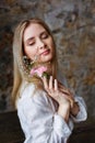 A beautiful young blonde woman holds carnation and gypsophila flowers in her hands near her face