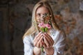 A beautiful young blonde woman holds carnation and gypsophila flowers in her hands near her face