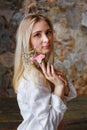 A beautiful young blonde woman holds carnation and gypsophila flowers in her hands near her face