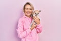 Beautiful young blonde woman hugging cute chihuahua dog winking looking at the camera with sexy expression, cheerful and happy Royalty Free Stock Photo