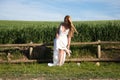 A beautiful young blonde woman with long hair in a wedding dress fastens her high heels while sitting on a wooden fence. In the Royalty Free Stock Photo