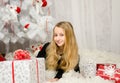 Beautiful young blonde woman lying in the new year with presents near the Christmas tree, studio shot