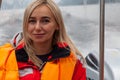 Beautiful young blonde woman in an orange life jacket sits in a motor boat during an excursion and sailing on Lake Teletskoye in