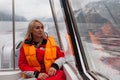 Beautiful young blonde woman in an orange life jacket sits in a motor boat during an excursion and sailing on Lake Teletskoye in
