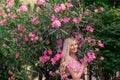 Beautiful young blonde woman in a pink dress stands posing outdoors near a bush with flowers. Royalty Free Stock Photo