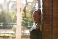 Beautiful young blonde woman with a ponytail in her hair leaning against a red brick wall and holding on to a fence. In the Royalty Free Stock Photo