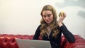 Beautiful young blonde woman on red sofa using laptop and eating a green apple in living room. Royalty Free Stock Photo