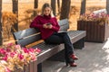 Beautiful young blonde woman in a red sweater sits on a bench with a smartphone. autumn concept