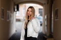 Beautiful young blonde woman with sexy lips in a black stylish sweater in a fashionable white winter jacket walks outdoors near a Royalty Free Stock Photo
