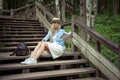 Beautiful young blonde woman sits on wooden steps in a city park with a book in hands. She is wearing a white dress, a Royalty Free Stock Photo