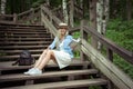 Beautiful young blonde woman sits on wooden steps in a city park with a book in hands. She is wearing a white dress, a Royalty Free Stock Photo