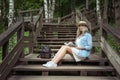 Beautiful young blonde woman sits on wooden steps in a city park with a book in hands. She is wearing a white dress, a Royalty Free Stock Photo