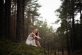 Beautiful young blonde woman sitting in forest nymph in white dress in evergreen wood Royalty Free Stock Photo
