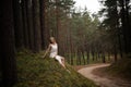 Beautiful young blonde woman sitting in forest nymph in white dress in evergreen wood Royalty Free Stock Photo
