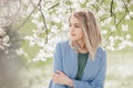 A beautiful young blonde woman standing near an apple tree in a green dress and a blue coat Royalty Free Stock Photo