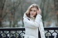 Beautiful young blonde woman standing on the spring city park in warm clothes. Cold season lifestyle freshness concept