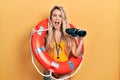 Beautiful young blonde woman wearing bikini and holding lifeguard float and binoculars celebrating crazy and amazed for success