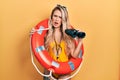 Beautiful young blonde woman wearing bikini and holding lifeguard float and binoculars in shock face, looking skeptical and Royalty Free Stock Photo