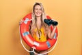 Beautiful young blonde woman wearing bikini and holding lifeguard float and binoculars winking looking at the camera with sexy Royalty Free Stock Photo