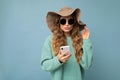 Beautiful young blonde woman wearing blue sweater hat and sunglasses standing isolated over blue background surfing on