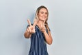 Beautiful young blonde woman wearing casual striped dress smiling looking to the camera showing fingers doing victory sign Royalty Free Stock Photo