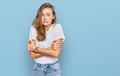 Beautiful young blonde woman wearing casual white t shirt shaking and freezing for winter cold with sad and shock expression on Royalty Free Stock Photo