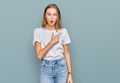 Beautiful young blonde woman wearing casual white t shirt surprised pointing with finger to the side, open mouth amazed expression Royalty Free Stock Photo