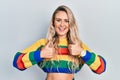 Beautiful young blonde woman wearing colored sweater success sign doing positive gesture with hand, thumbs up smiling and happy Royalty Free Stock Photo