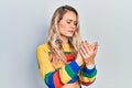 Beautiful young blonde woman wearing colored sweater suffering pain on hands and fingers, arthritis inflammation