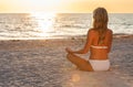 Beautiful young blonde woman in a white bikini sitting on a beach at sunset Royalty Free Stock Photo